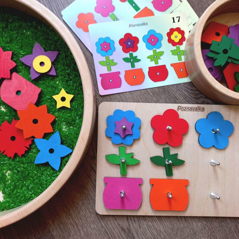 May include: A wooden flower puzzle with three different colored flowers and pots. The puzzle pieces are on a wooden board with the word "Poznavalka" written on it. The puzzle is designed for children to learn about colors and shapes.