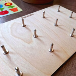 May include: A wooden board with the word "Poznawika" printed on it. The board has ten silver metal pegs with round heads.