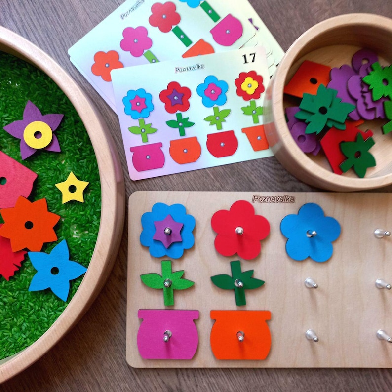 May include: A wooden flower puzzle with three flower shapes, each with a different colored center. The puzzle pieces are on a wooden board with the word "Poznavaka" printed on it. The puzzle is designed for children to learn about colors and shapes.
