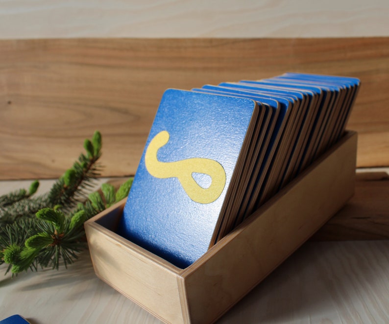 May include: A wooden box filled with blue cards, each with a yellow letter or shape on it. The box is sitting on a wooden surface.