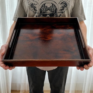 Op de afbeelding: Een rechthoekig houten dienblad met een diepbruine afwerking. Het dienblad heeft een glad, gepolijst oppervlak en geïntegreerde handgrepen aan weerszijden. De houtnerf is zichtbaar, wat bijdraagt aan de natuurlijke uitstraling.
