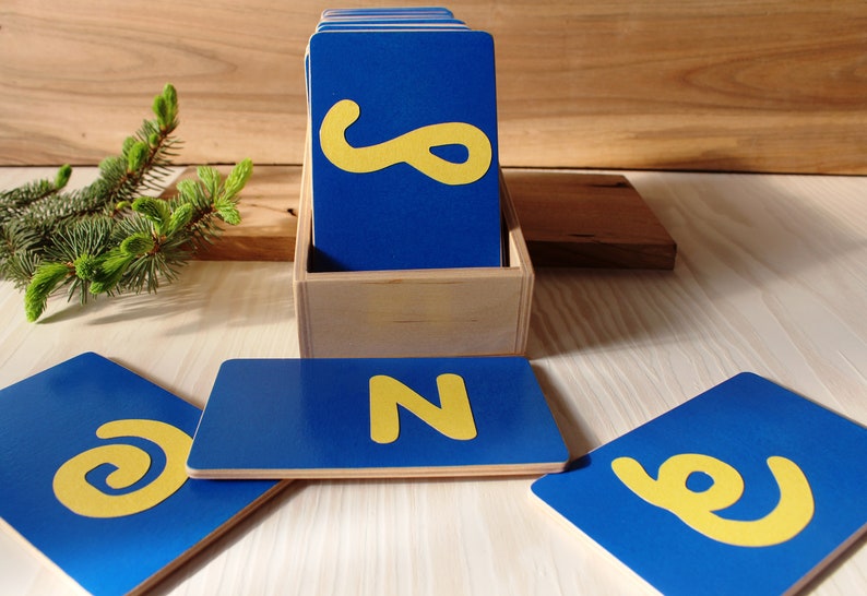 May include: A set of blue wooden alphabet cards with yellow letters. The cards are in a wooden box. The letters are N, e, and g.