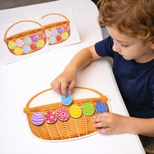 Peut inclure: Un enfant joue avec un jeu d'association d'œufs de Pâques colorés. Le jeu comprend un plateau en forme de panier et plusieurs pièces en forme d'œuf avec divers motifs. Une image imprimée de deux paniers de Pâques est en arrière-plan.