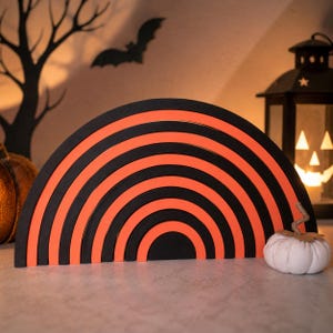 Könnte beinhalten: Ein halbkreisförmiges Stapelspielzeug mit abwechselnden konzentrischen Bögen in Schwarz und leuchtendem Orange. Das Objekt besteht aus mehreren ineinandergreifenden, gebogenen Teilen, die zusammengefügt eine vollständige Regenbogenform bilden.