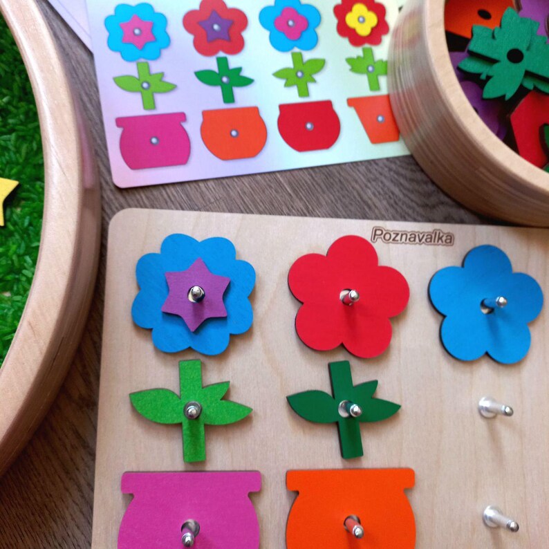 May include: A wooden puzzle board with the word "Poznavalka" printed on it. The puzzle features three flower shapes with stems and pots. The flower shapes are blue, red, and green. The stems are green and the pots are pink, orange, and purple.