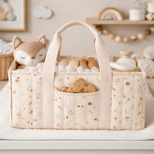 May include: A cream-colored baby caddy with a floral and mushroom pattern, featuring a plush fox toy, wooden toys, and baby essentials. The caddy has a pocket and sturdy handles for easy carrying.