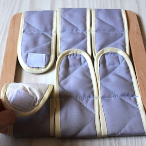 Puede incluir: Un marco de madera con seis cuadrados de tela gris con ribete amarillo y cierres de velcro. Los cuadrados son extra&iacute;bles y se pueden organizar en diferentes patrones.