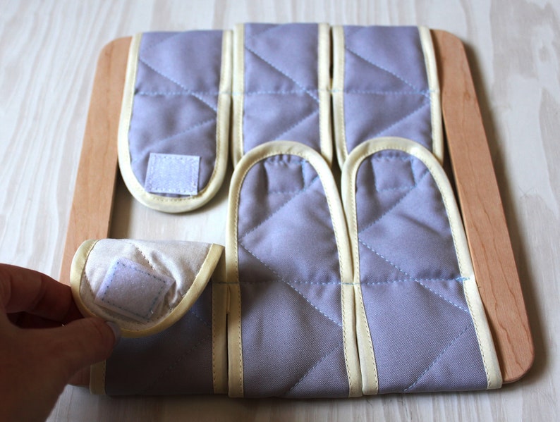 Puede incluir: Un marco de madera con seis cuadrados de tela gris con ribete amarillo y cierres de velcro. Los cuadrados son extra&iacute;bles y se pueden organizar en diferentes patrones.