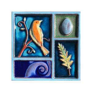 May include: A square ceramic tile with a light blue border, featuring four distinct sections. One section depicts an orange bird perched on a branch. Other sections show an egg, a fern, and a blue swirl design. The tile has a glossy finish.