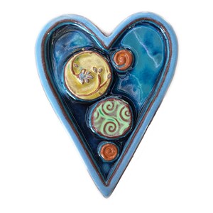 May include: A blue ceramic heart-shaped wall hanging with a textured surface and three colorful circles with swirls and floral designs.