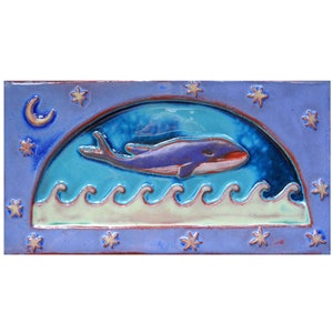 May include: A blue and purple whale swims under a crescent moon and stars in a blue and white ocean. The whale is in a ceramic tile with a blue background.