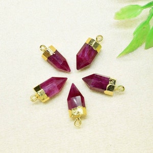 Może przedstawiać: Pięć pozłacanych zawieszek z fasetowanym, szpiczastym, rubinowo-czerwonym kamieniem szlachetnym. Każda zawieszka ma pętelkę u góry do przymocowania do naszyjnika lub bransoletki.