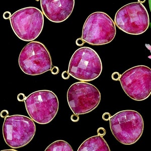May include: A collection of pink gemstone pendants with gold-toned metal loops. The gemstones are faceted and have a teardrop shape.