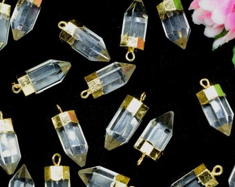 May include: A collection of clear crystal point pendants with gold-toned metal caps and jump rings. The pendants are scattered on a black surface.