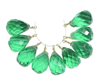 Op de afbeelding: Een streng van tien gefacetteerde groene, traanvormige kristallen kralen met goudkleurige draadlussen.