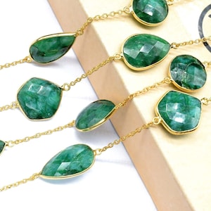 May include: A gold chain necklace with emerald green gemstone drops and faceted stones. The necklace is layered and features a variety of shapes and sizes of stones.