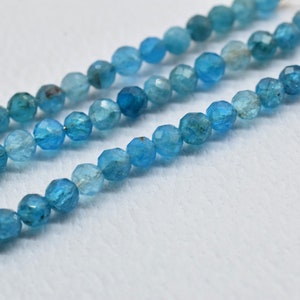 Puede incluir: Primer plano de tres hilos de cuentas de piedras preciosas azul claro. Las cuentas redondas están facetadas, creando un efecto brillante. El color es azul claro y vibrante. Ideal para la creación de joyas.