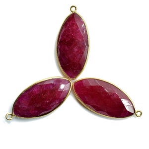May include: Three maroon gemstone pendants with gold settings. The gemstones are oval shaped and have a faceted finish.