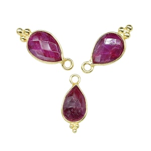 Könnte beinhalten: Drei goldfarbene Anhänger in Tropfenform mit roten Edelstein-Akzenten. Jeder Anhänger hat eine kleine Öse zum Anbringen an einer Kette oder anderem Schmuck.