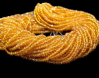 May include: A close-up of a large spool of golden yellow glass beads. The beads are small and round, and they are arranged in a tight coil.