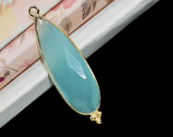 May include: A light blue teardrop-shaped gemstone pendant with a gold setting. The pendant is on a white and pink floral background.
