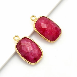 Puede incluir: Dos colgantes de color dorado con una piedra preciosa roja de forma rectangular.