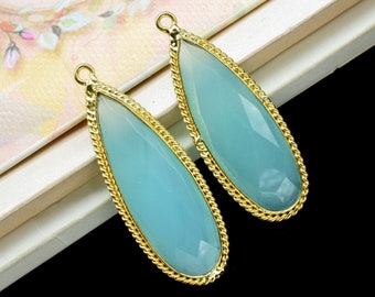 May include: Two teardrop-shaped turquoise blue glass pendants with gold-toned metal frames. The pendants have a rope-like design around the edges.