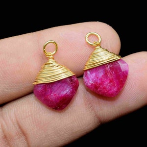 May include: Two pink gemstone pendants with gold wire wrapped around them. The pendants are shaped like a teardrop and have a shiny finish.