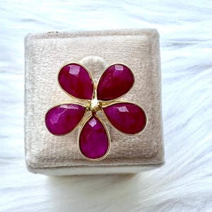 May include: A gold ring with a pink flower design. The flower has five petals and a gold center.