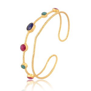 May include: A gold bangle bracelet with a double band design. The bracelet is adorned with five gemstones: two pink, two green, and one blue.