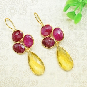 Puede incluir: Un par de pendientes de oro con piedras preciosas amarillas en forma de lágrima y tres piedras preciosas rosas redondas.