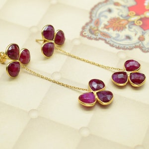 May include: A pair of gold earrings with three ruby-colored stones each, hanging from a delicate gold chain.