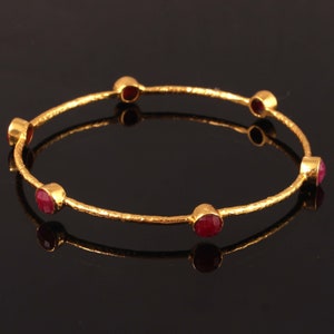 May include: A gold bangle bracelet with seven red gemstones set into the metal. The bracelet has a hammered texture.