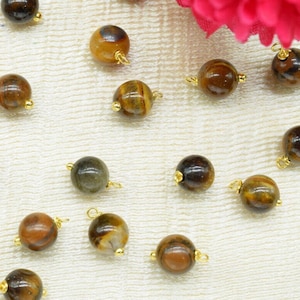 May include: A collection of round, gold-toned beads with a tiger's eye pattern. The beads are arranged on a white fabric surface.