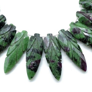 May include: A strand of green and purple gemstone beads carved into leaf shapes. The beads are strung on a silver wire.