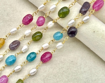 Puede incluir: Primer plano de varias hebras de collares con cadenas doradas. Cada hebra presenta una combinación de perlas blancas y piedras preciosas ovaladas de colores en tonos rosa, verde, azul y morado. Los collares se muestran sobre un fondo neutro.