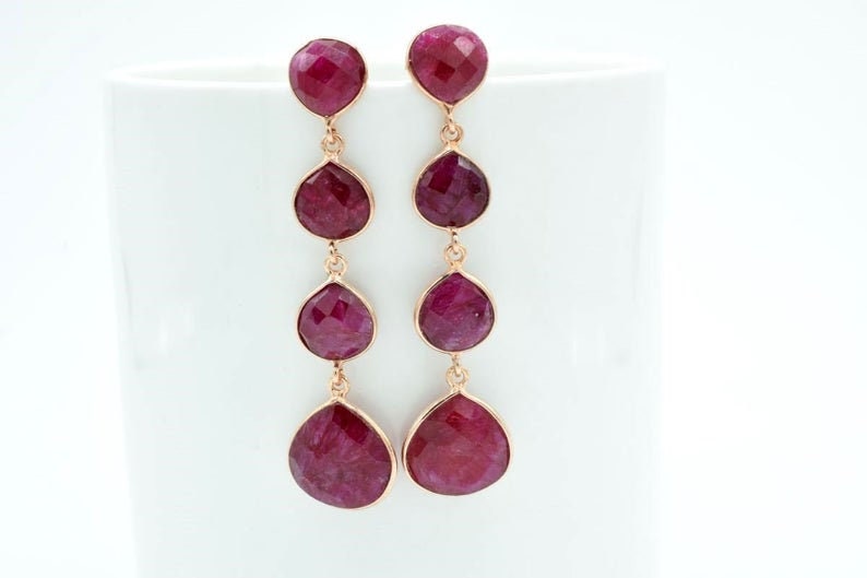 May include: A pair of long, dangling earrings with four faceted, teardrop-shaped, pink gemstones on each earring.