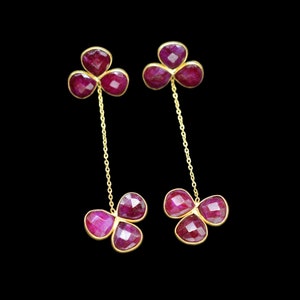 May include: A pair of gold earrings with three ruby-colored stones on each earring. The stones are connected by a gold chain.