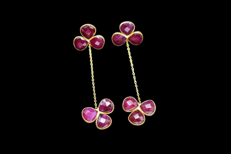 May include: A pair of gold earrings with three ruby-colored stones on each earring. The stones are connected by a gold chain.