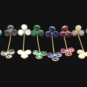 May include: A set of ten pairs of dangle earrings featuring a clover design with different colored gemstones. The earrings are made of gold and feature a chain connecting the two clover designs.