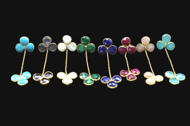 May include: A set of ten pairs of dangle earrings featuring a clover design with different colored gemstones. The earrings are made of gold and feature a chain connecting the two clover designs.