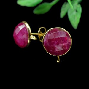 May include: A pair of gold earrings with red gemstone accents. The earrings have a round shape and a faceted design.
