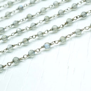 May include: A silver chain with grey gemstone beads. The chain is made of small, delicate links and the beads are round and faceted.