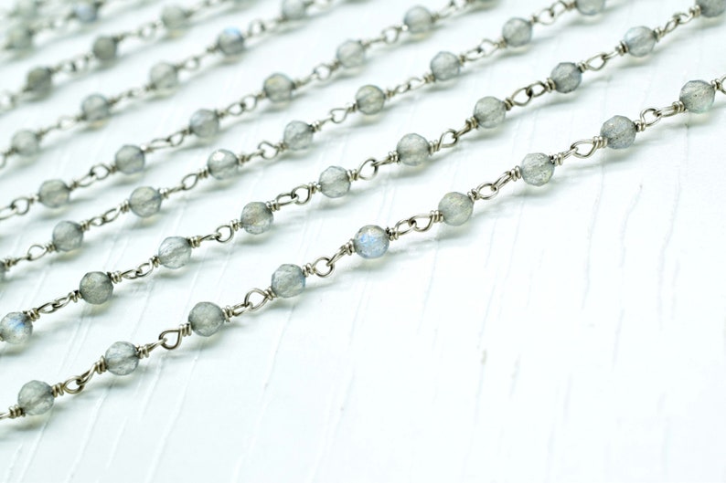 May include: A silver chain with grey gemstone beads. The chain is made of small, delicate links and the beads are round and faceted.