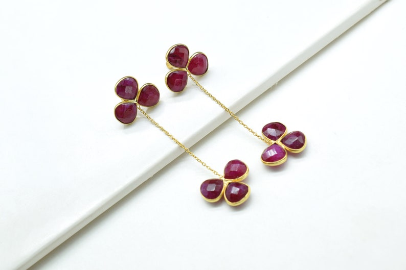May include: A pair of gold earrings with three ruby-colored stones on each earring. The stones are connected by a gold chain.