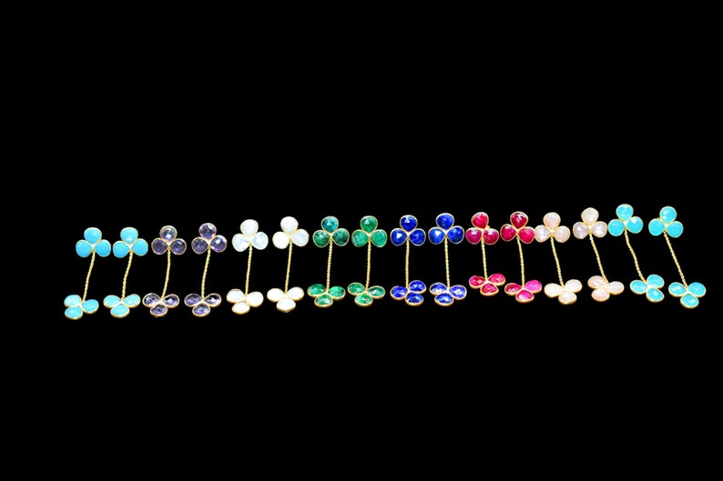 May include: A set of 16 pairs of dangle earrings featuring a clover design with different colored gemstones. The earrings are made of gold metal and have a delicate chain.
