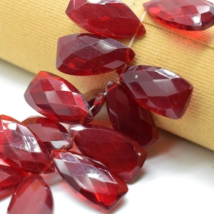 May include: A strand of faceted, red glass beads. The beads are shaped like teardrops and have a glossy finish.