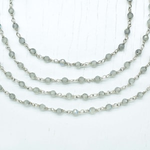 May include: A layered necklace with five strands of silver chain and grey gemstone beads.