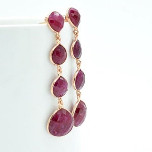 May include: A pair of long, dangling earrings with multiple teardrop-shaped ruby stones. The earrings are made of gold and feature a delicate chain design.