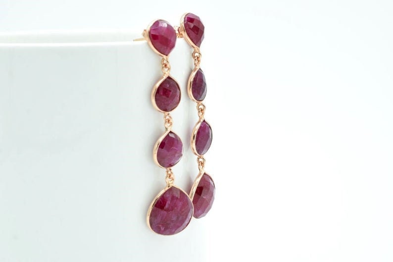 May include: A pair of long, dangling earrings with multiple teardrop-shaped ruby stones. The earrings are made of gold and feature a delicate chain design.